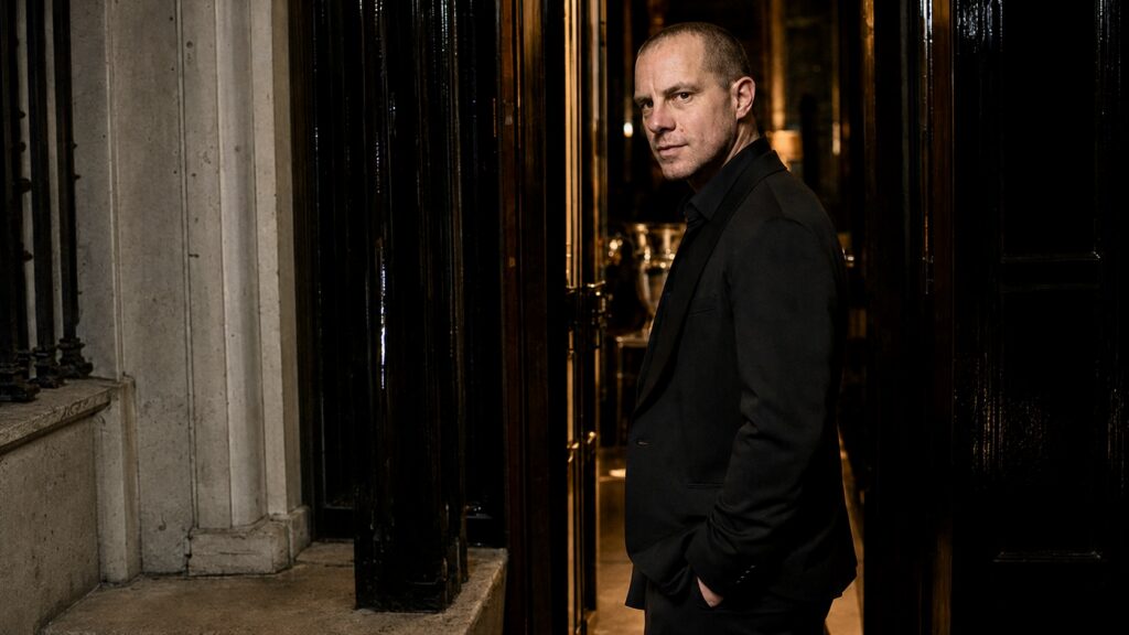 Barry Roberts standing in the entrance of a grand London townhouse at night.